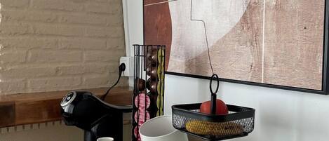 Una encimera de cocina con una cafetera, una frutera y una bandeja con diversos objetos.