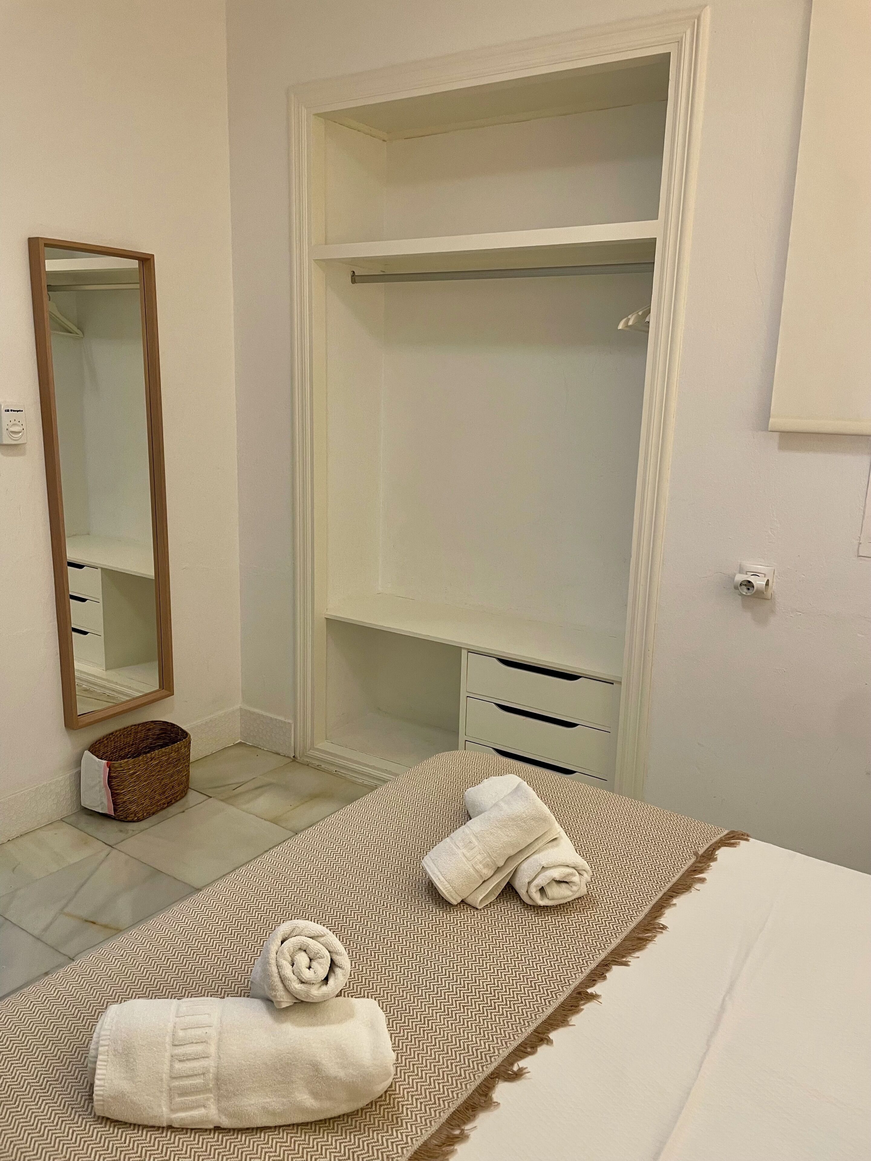 Un dormitorio con cama, un armario grande, un espejo y una pequeña cesta de mimbre.
