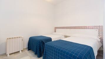 Two single beds with blue checkered bedspreads are positioned against a wall with a decorative headboard.