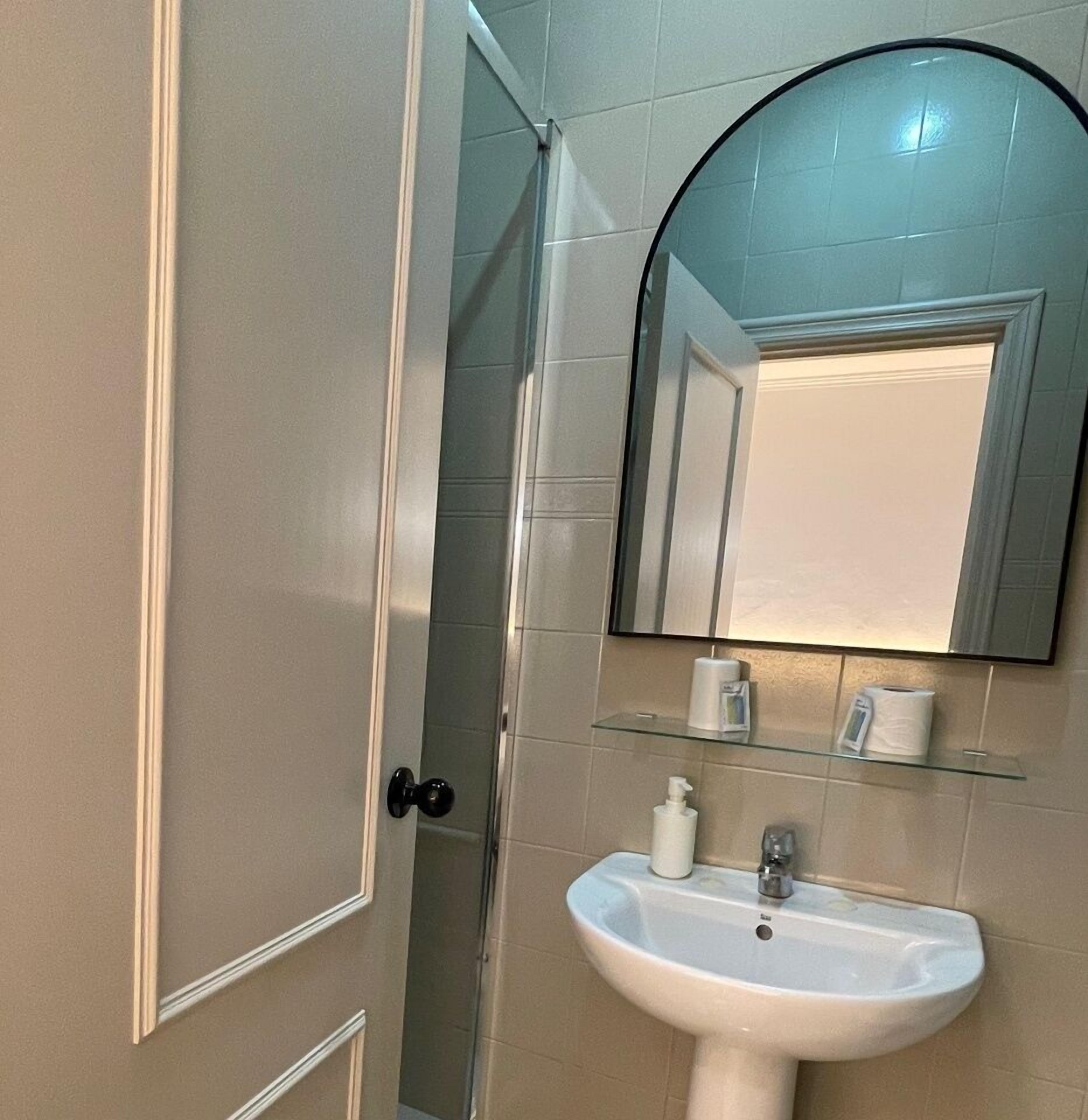 Une salle de bain avec un lavabo blanc, un miroir et une porte.