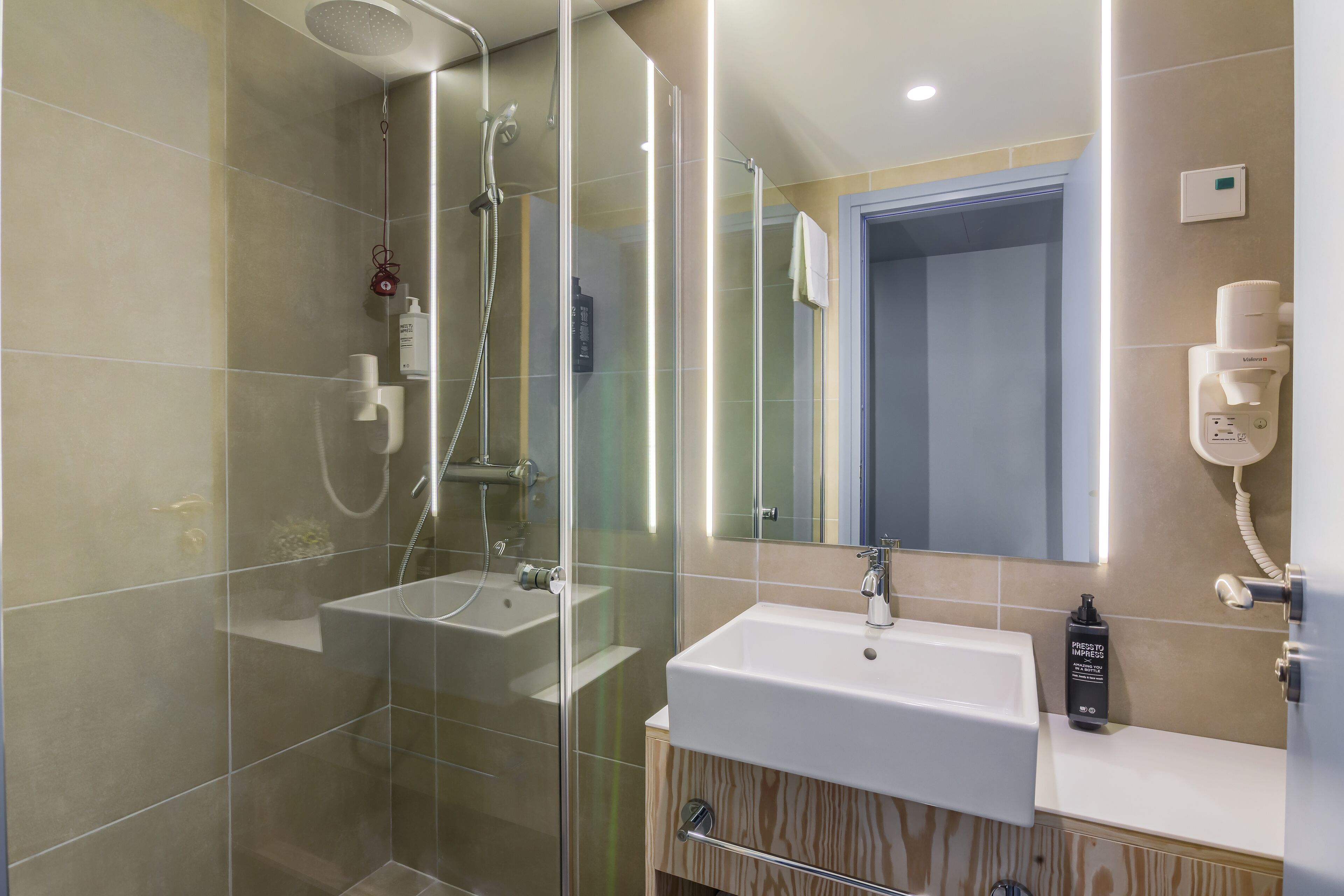 A modern bathroom with a glass-enclosed shower, a standalone sink, and a mirror with integrated lighting.