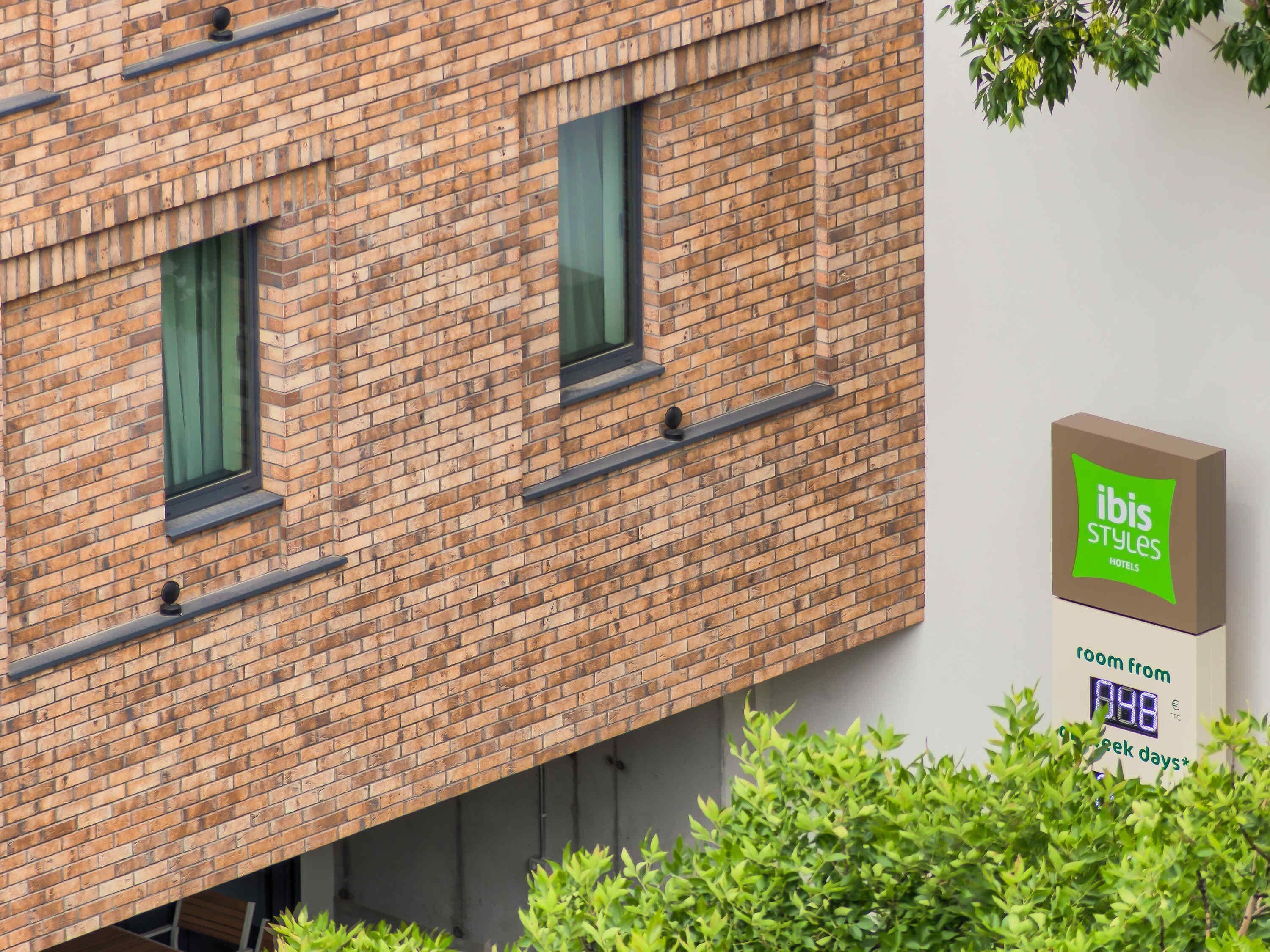 Un bâtiment en briques sur lequel est apposée une enseigne indiquant qu’il s’agit d’un hôtel ibis Styles, et précisant que des chambres sont disponibles du 4 au 9 juin.