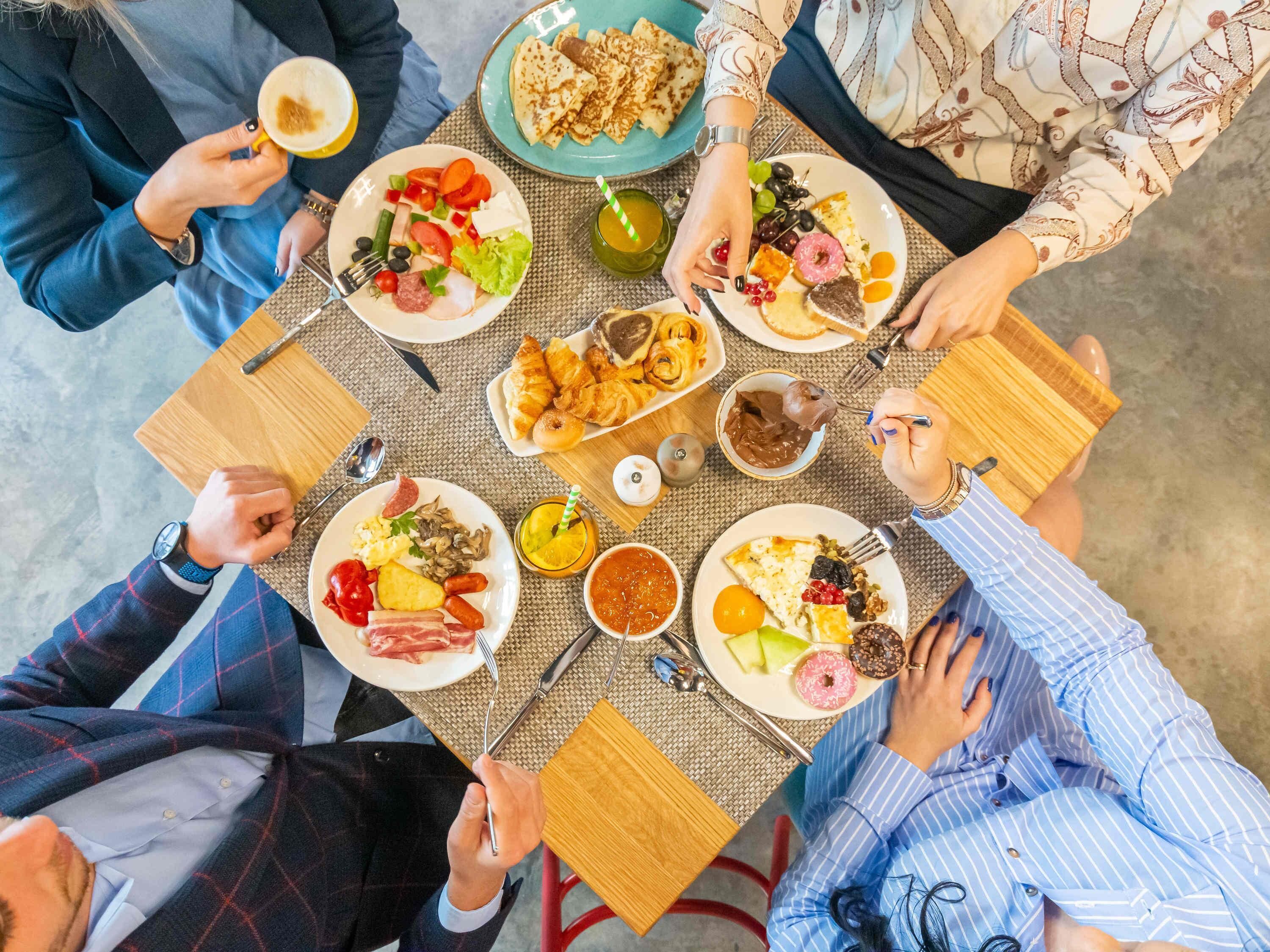 A group of people dining around a table with various dishes, including croissants, salads, and desserts.