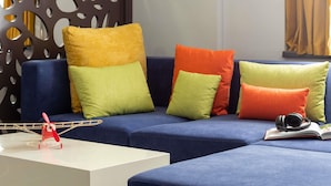Un salon moderne avec un canapé bleu, des coussins colorés, une table basse blanche et un élément de séparation décoratif orné de motifs découpés.