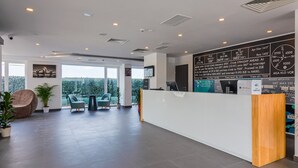 Un espace d’accueil moderne, doté d’un comptoir de réception blanc, d’un grand écran numérique et offrant une vue sur le paysage urbain grâce à de grandes fenêtres.