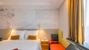 Habitación de hotel con un mapa grande en la pared, una cama con ropa de cama blanca, una mesita pequeña y una ventana con cortinas.