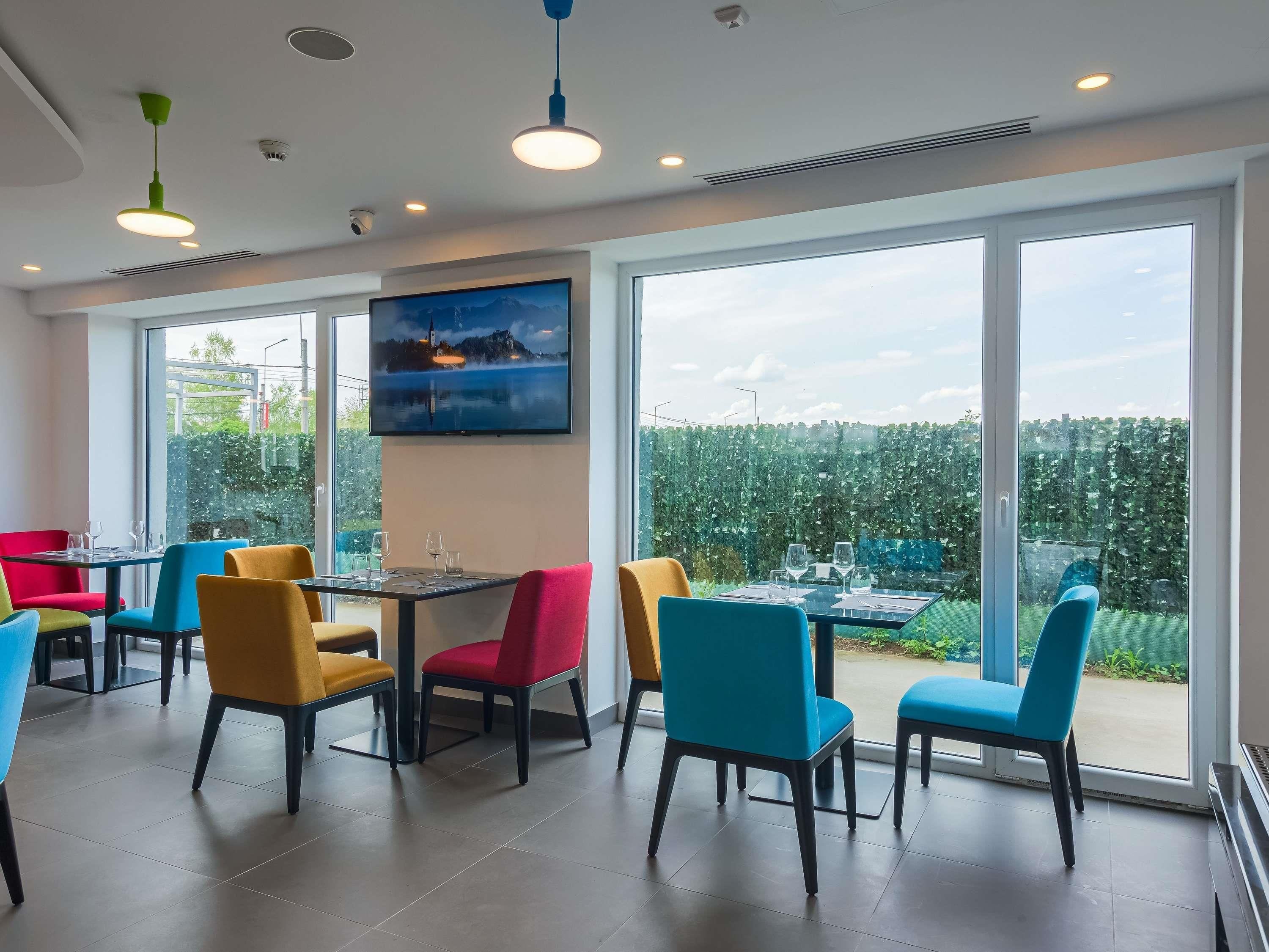 Uma sala de jantar moderna com grandes janelas, um quadro e cadeiras coloridas.