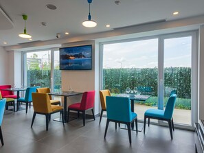 Un espace de restauration moderne avec de grandes fenêtres, un tableau et des chaises colorées.
