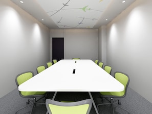 A conference room with a long table, green chairs, a black door, and a ceiling with airplane decals.