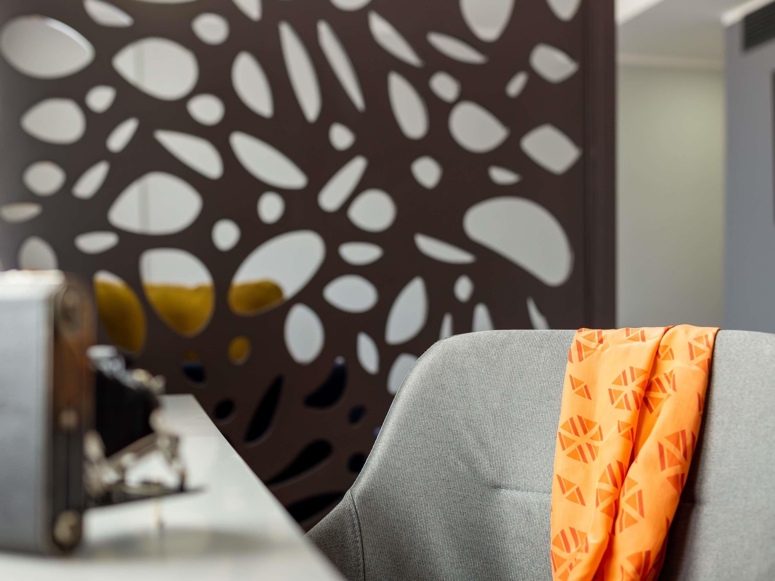 A room with a grey sofa, an orange patterned throw, and a decorative wall with abstract shapes.