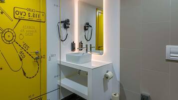 Un baño moderno con una puerta amarilla, un lavabo blanco, un espejo y un dispensador de papel higiénico.