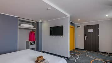 Una habitación de hotel con cama, televisor montado en la pared, armario, perchero y puerta.