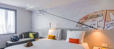 A hotel room with a large bed, a desk, a chair, and a map on the wall.