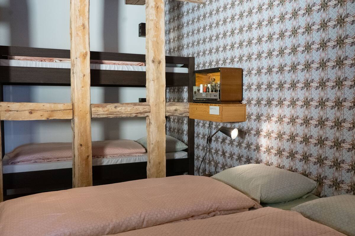 Habitación con literas, cabecera de madera, estante pequeño con espejo y papel tapiz estampado.