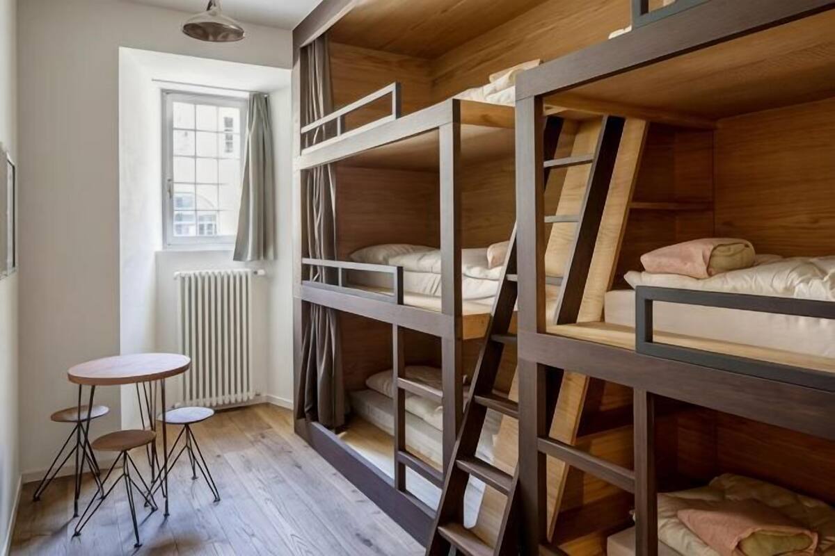 Dormitorio con literas, ventana, radiador y una mesita.