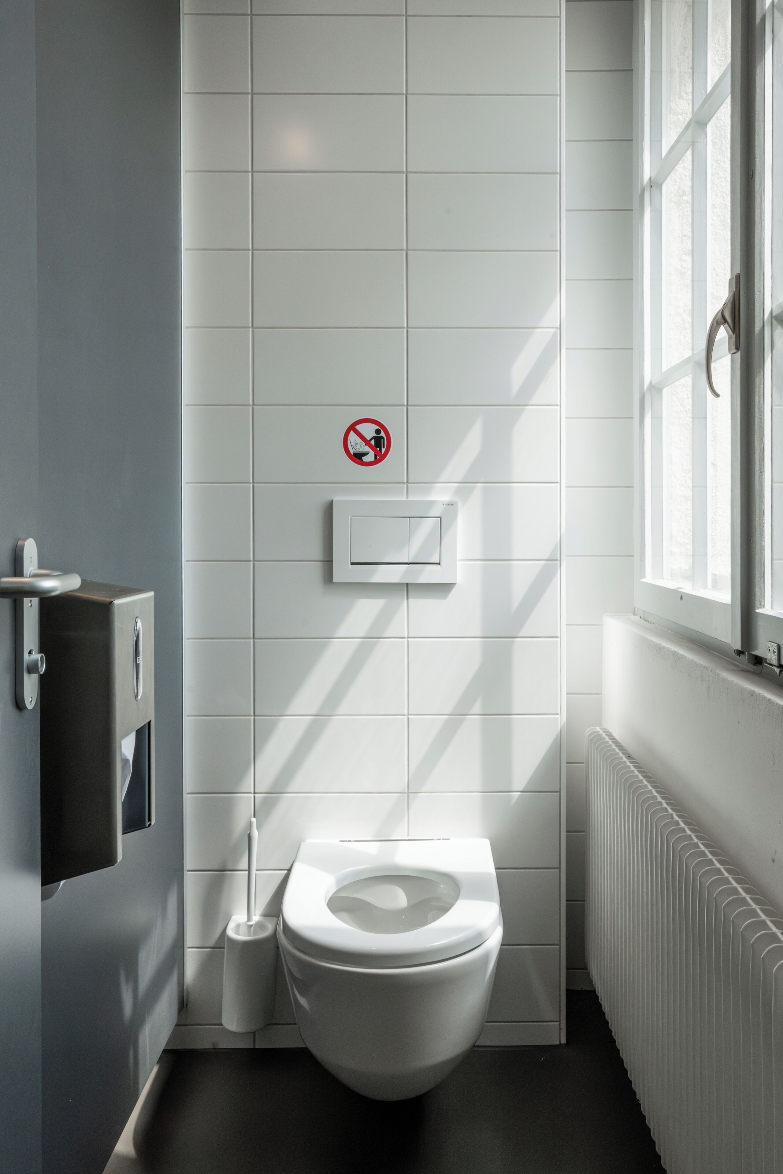 A modern bathroom with a toilet, a hand dryer, and a no-smoking sign.