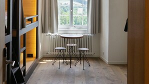 Een kamer met een groot rondboogvenster, een ronde tafel met vier stoelen, een hanglamp en een radiator onder het raam.