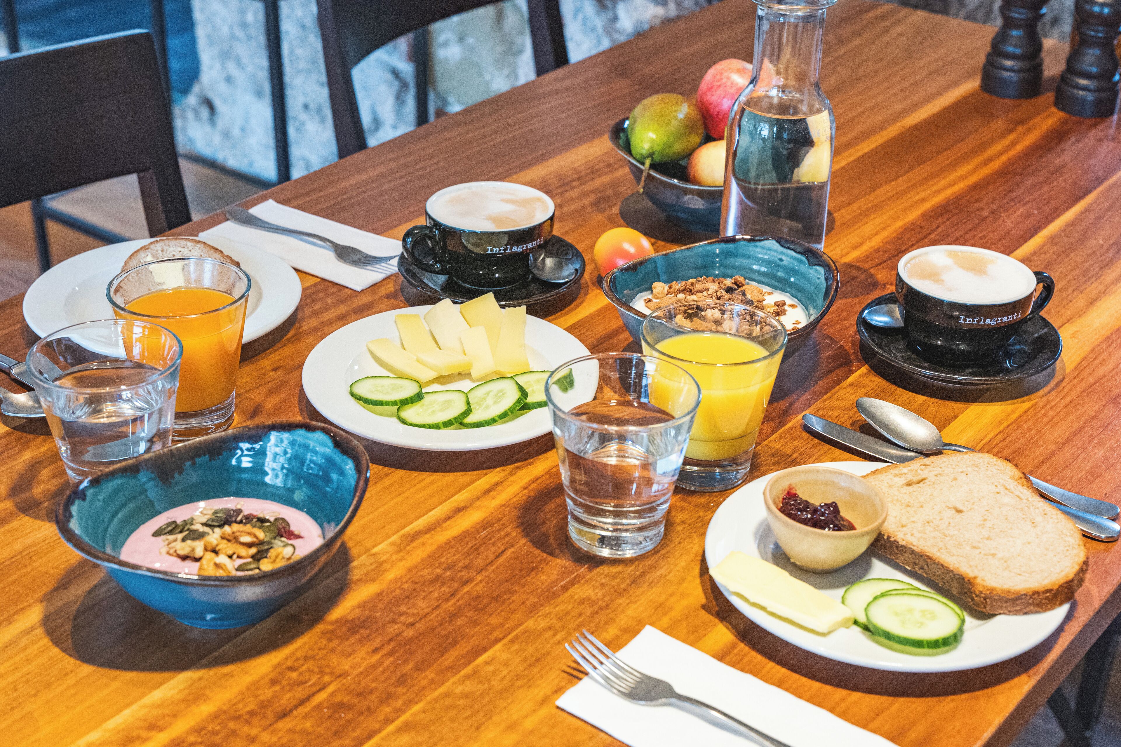 A wooden dining table with breakfast items including toast, fruit, cereal, and beverages.