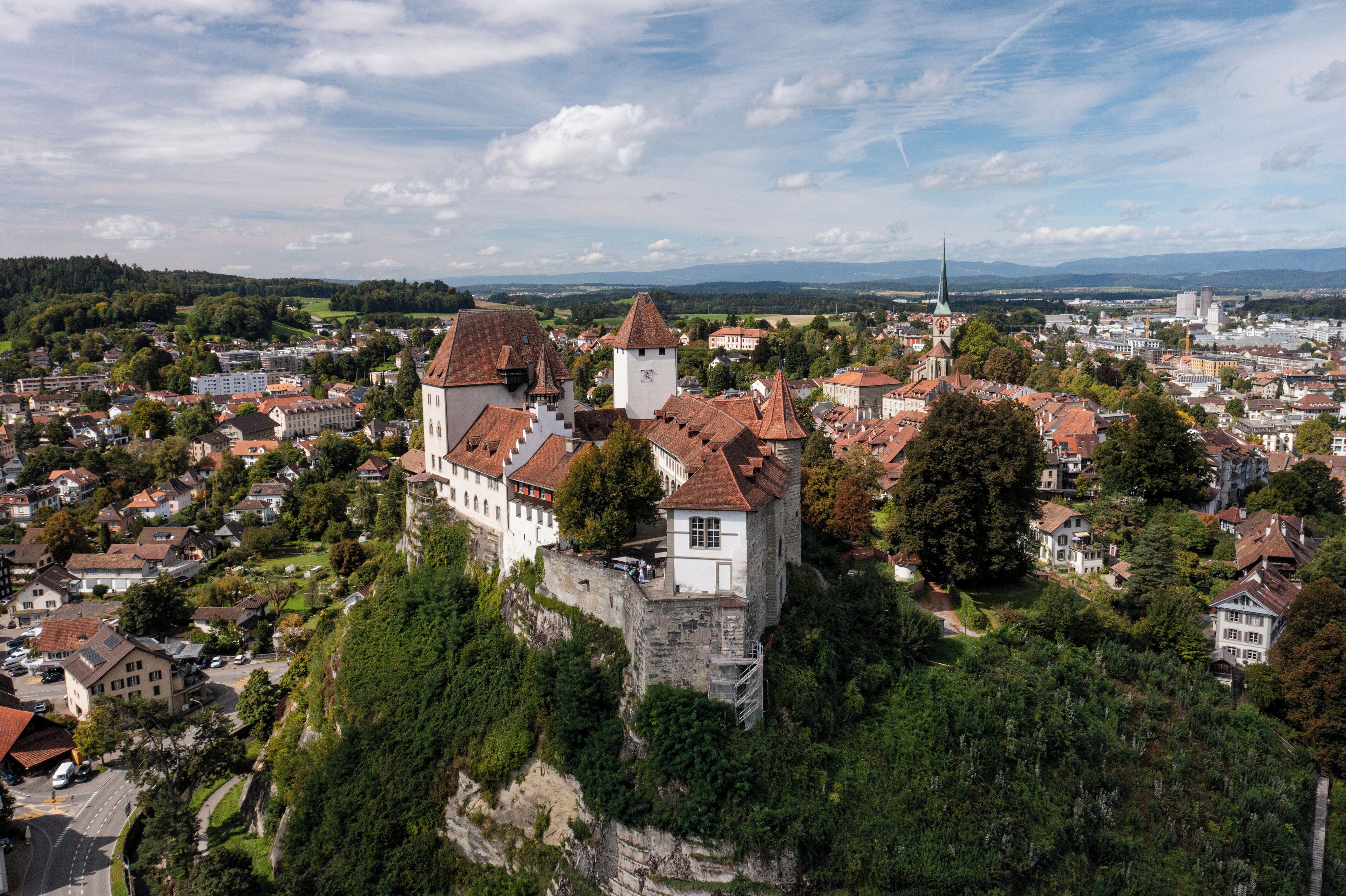 Un castillo histórico en una colina con vistas a un pueblo de edificios con tejados rojos y la aguja de una iglesia a lo lejos.