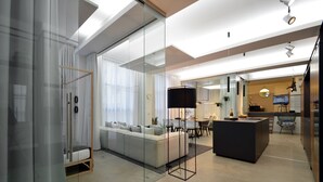 A modern living room with a glass partition, a sofa, a dining area, and a kitchen with a TV.