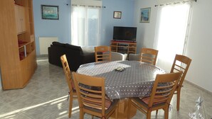 A living room with a round dining table, wooden chairs, a black sofa, a TV stand, and a wooden cabinet. - Charming F3 house in Saujon, 2 bedrooms, pets allowed, parking (Saujon)