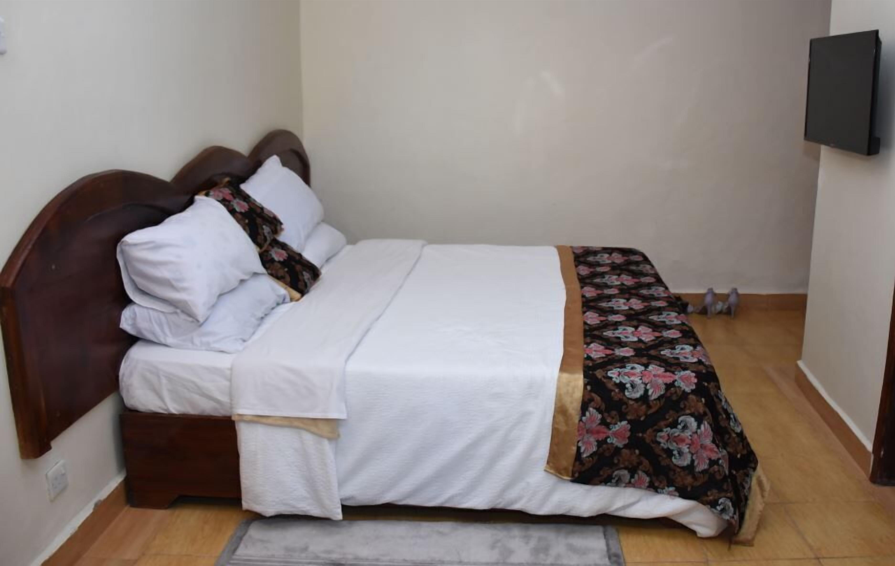 Un lit simple avec une tête de lit en bois, du linge de lit blanc et une couvre-lit à motifs floraux.