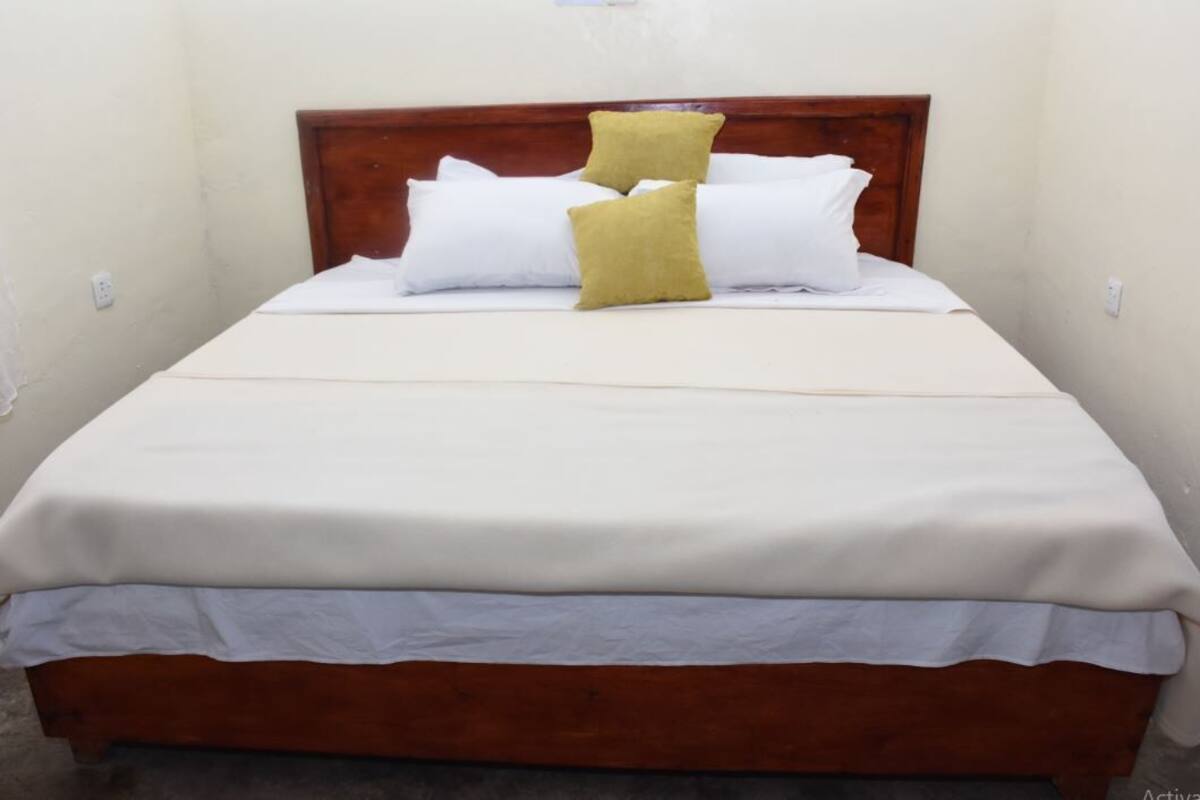 A single bed with a wooden headboard, white bedding, and two pillows.
