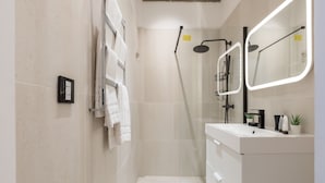 Ein modernes Badezimmer mit einer gläsernen Duschkabine, einem weißen Waschtisch und einem Spiegel mit integrierter Beleuchtung.