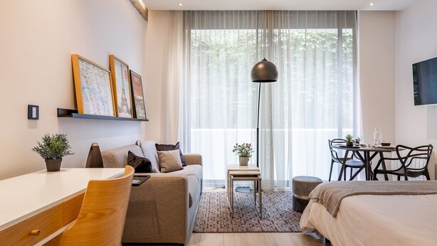 Ein modernes Hotelzimmer mit einer Couch, einem Schreibtisch, einem Esstisch und einem Bett.