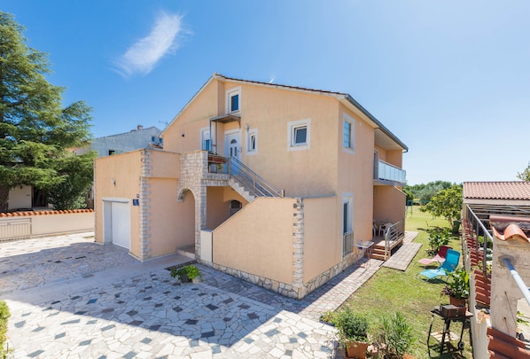 A two-story house with a stone-paved courtyard, a small staircase, and a balcony.