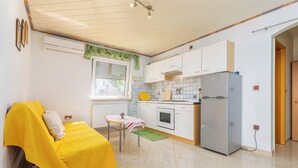 Una cocina compacta con armarios blancos, un refrigerador gris y una pequeña mesa de comedor con mantel amarillo.