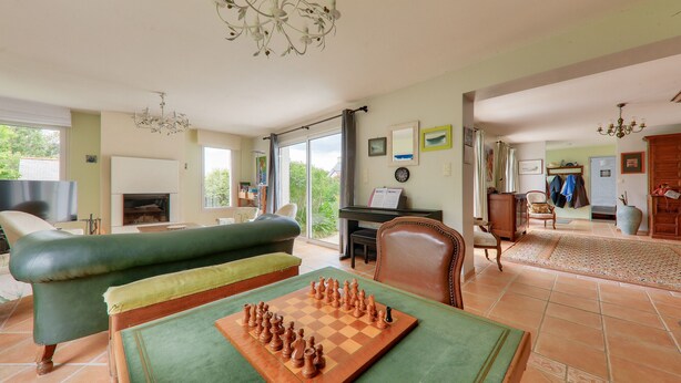 Una sala de estar con un tablero de ajedrez, un sofá verde, un piano y un comedor.