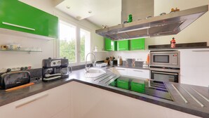 Cocina moderna con gabinetes verdes, extractor de acero inoxidable, cafetera, tostadora y microondas.