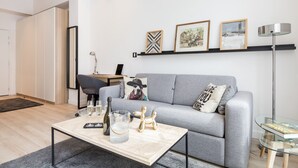 A modern living room with a grey sofa, a glass coffee table, and a desk with a computer. There are framed pictures on the wall and a floor lamp. - A3 Suite Studio 175Blo-Paris Convention (Paris-15E-Arrondissement)