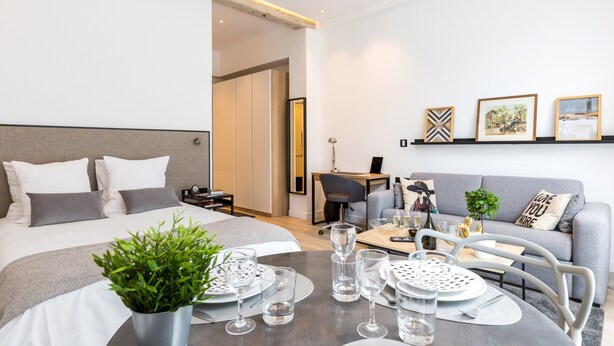 A modern hotel room with a neatly made bed, a dining table set for two, a sofa, and a desk with a chair. - A3 Suite Studio 175Blo-Paris Convention (Paris-15E-Arrondissement)