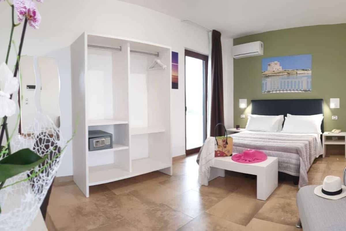 A hotel room with a bed, a sofa, a TV, a wardrobe, and a plant.