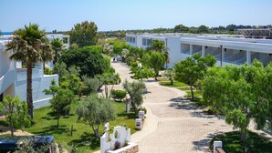 A modern hotel with a paved walkway, palm trees, and a clear view of the sea. - Torre Guaceto Greenblu Resort (Carovigno)