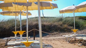 Beach umbrellas and lounge chairs arranged on a sandy beach with grass in the background. - Torre Guaceto Greenblu Resort (Carovigno)