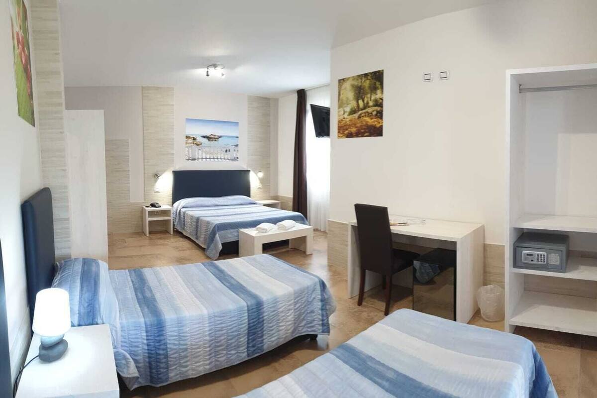 A hotel room with two beds, a desk, a chair, a wardrobe, and a small table with a lamp.