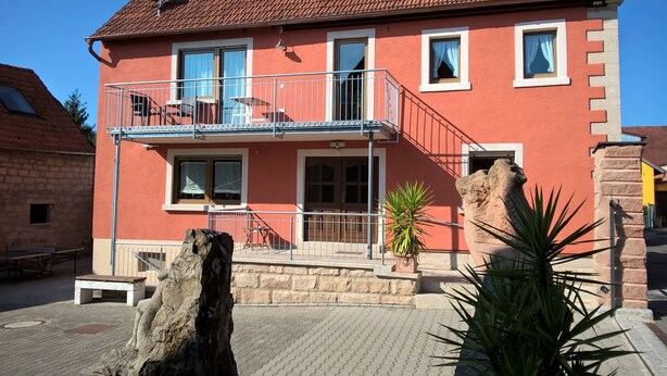 A red two-story building with a balcony, a stone staircase, and a rock sculpture in the foreground.