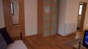 A bedroom with wooden flooring, a bed, a wardrobe, a television, and a small table with a bottle and glasses.