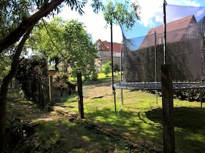 A garden with a trampoline, trees, and a house in the background. - Pension Atelier Reinhart (Rauhenebrach)