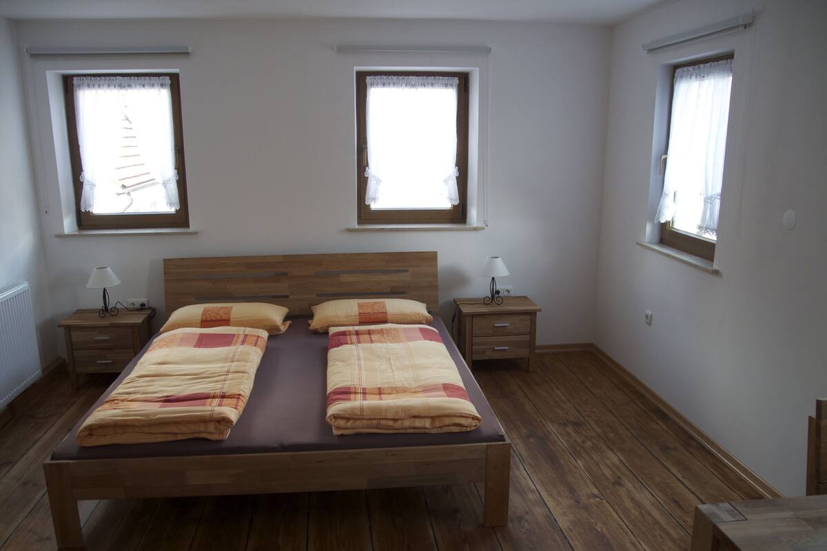 A bedroom with a wooden bed, two bedside tables, and two windows with curtains.
