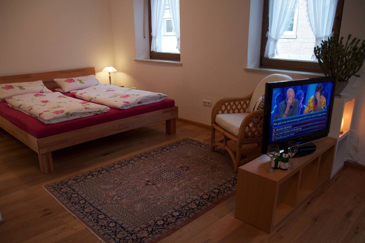 A bedroom with a bed, a television, a chair, and a window.