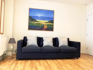 Relax in this stylish living room with a sofa, side table, and lamp, surrounded by a beautiful landscape painting.