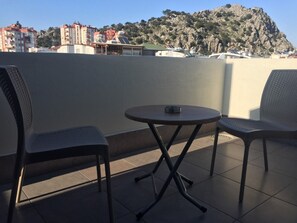 A terrace with two chairs and a table, overlooking a rocky hillside with buildings in the background. - Golden World Suite Hotel (Konyaalti)