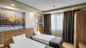 A hotel room with two beds, wooden headboards, a large landscape painting, a wardrobe, and a window with curtains. - Golden World Suite Hotel (Konyaalti)