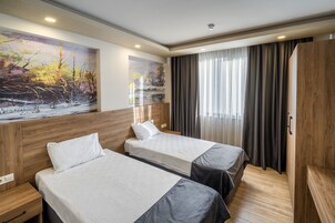 A hotel room with two beds, wooden headboards, a large landscape painting, a wardrobe, and a window with curtains.