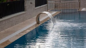 A swimming pool with a curved water feature, a metal railing, and a stone wall. - Golden World Suite Hotel (Konyaalti)