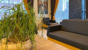 A modern living room with a large potted plant, a sofa, and a painting on the wall. - Golden World Suite Hotel (Konyaalti)